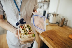 A nurse in uniform holding a plastic lunch box with a healthy wrap. The picture does not show their face.