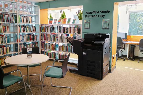 Library bookshelves behind a round table and photocopier