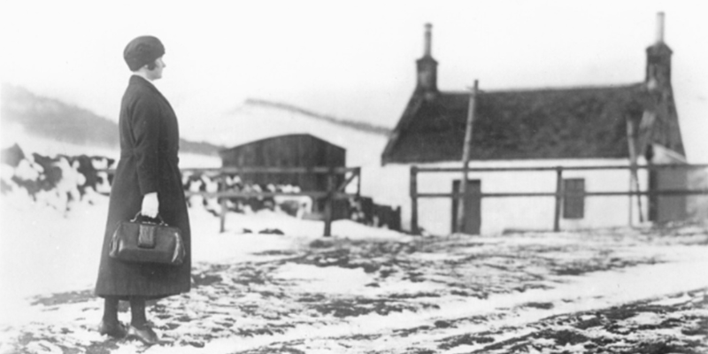 black and white photo of nurse outside a cottage