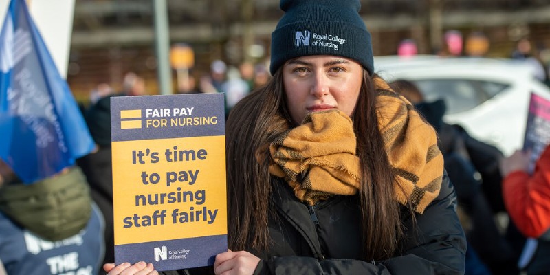 Person on picket line holding a sign saying It's time to pay nursing staff fairly