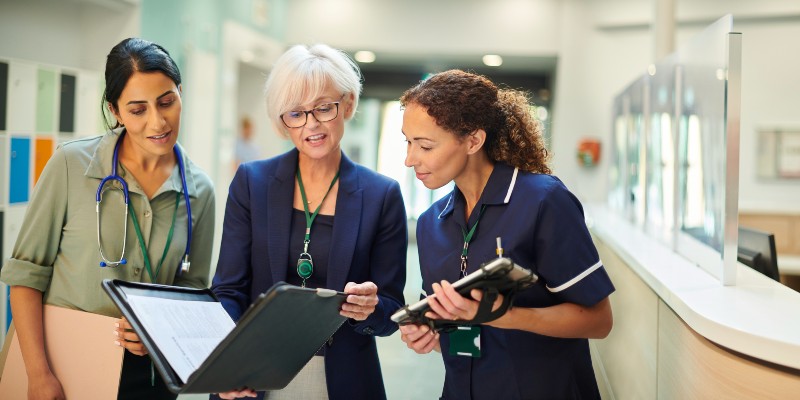 Three female staff, one in a nurse uniform, looking at a folder in a health care environment