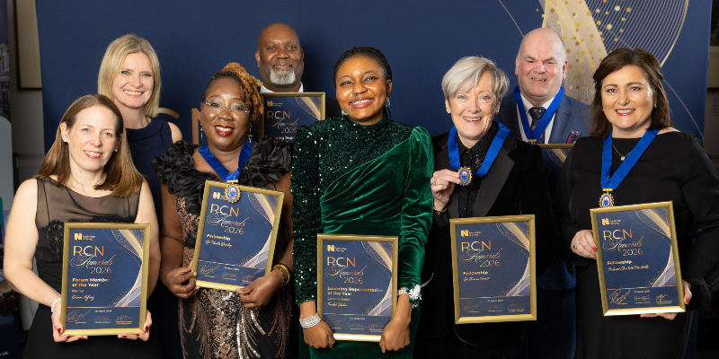 Eight people are shown at the RCN Awards 2026. They are all winners, wearing evening dresses and suits. All are holding their placards and awards, and smiling, looking directly into the camera