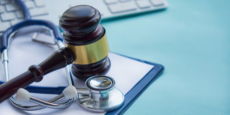 A gavel hits a clipboard with a stethoscope on it