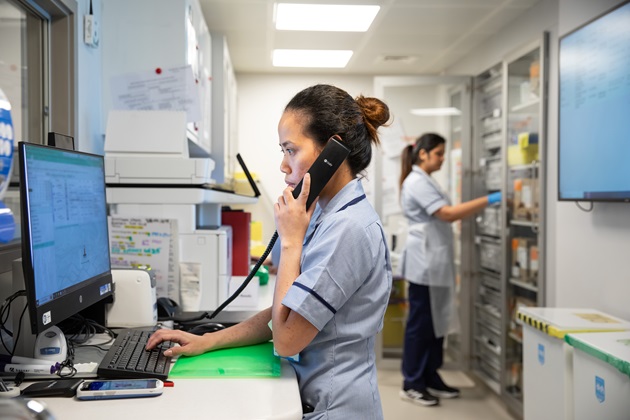 nurse in hospital ward speaking on phone next to a pc screen