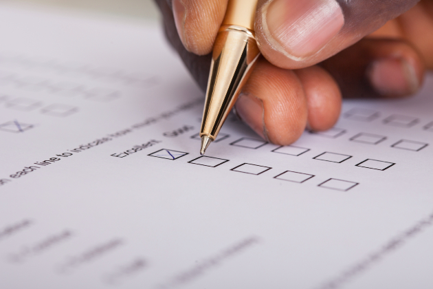 A hand is seen close up holding a metallic pen and filling in a job evaluation form with tick boxes.
