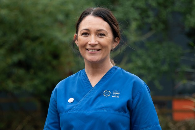 Tara Rees wearing blue scrubs, headshot outside against blurry tree background