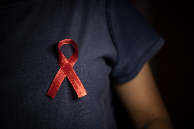A close up shows a red World Aids Day ribbon pinned on a person's dark blue nursing uniform