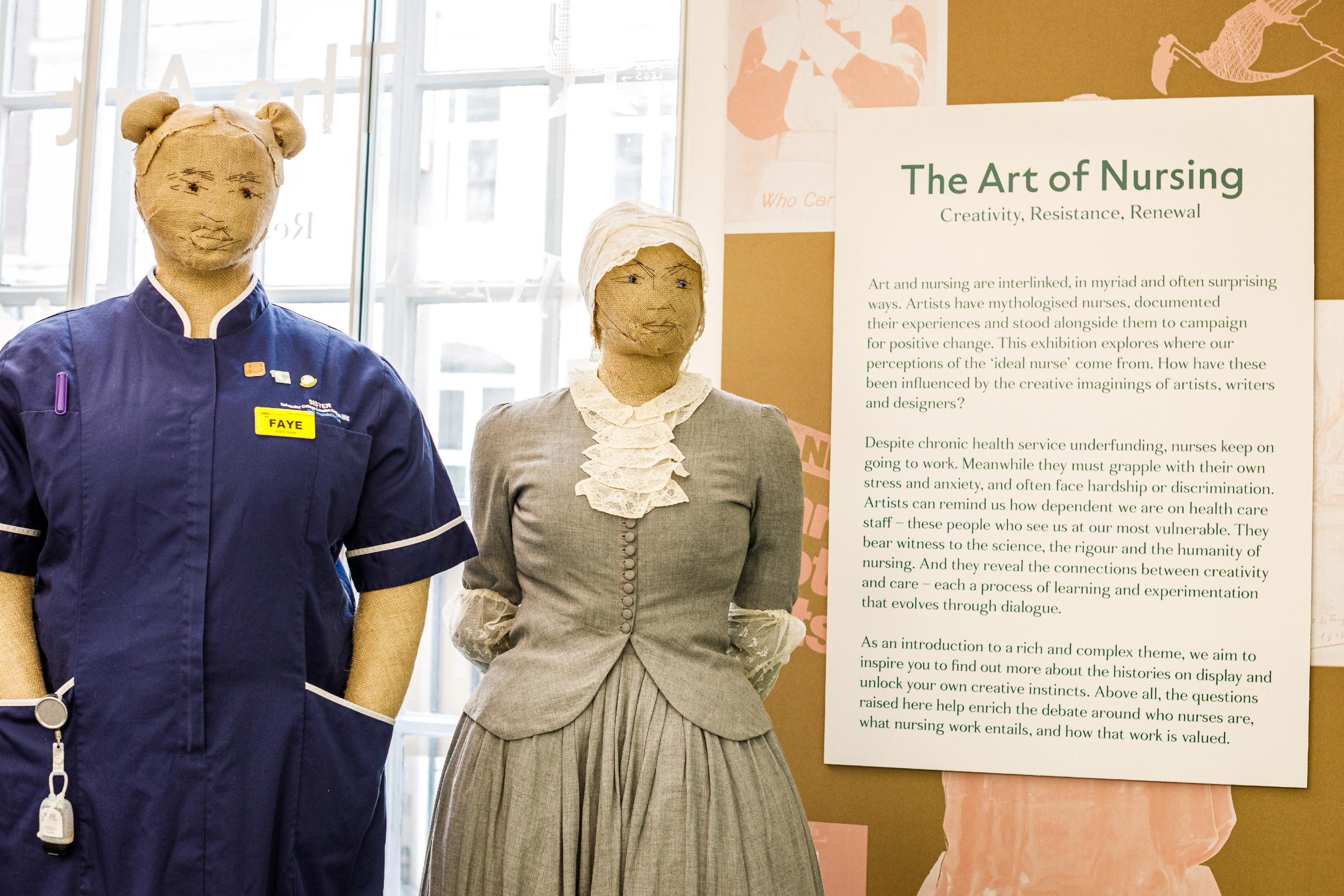 The art piece "Mannequins by Charlotte Mann" is shown. Two knitted mannequins wearing nursing uniforms stand side by side, next to a plaque introducing the exhibition, The Art of Nursing. The figure on the left wears a modern, blue uniform with the name tag "Faye". The figure on the right wears a traditional uniform in grey with a white head scarf and lacey neck piece.