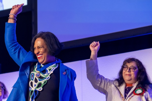 Two smiling women standing on a stage with their fists raised