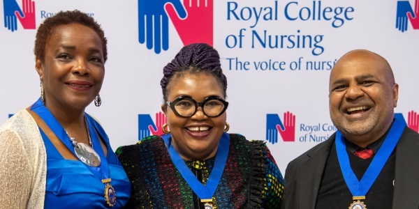 Three smiling people wearing medals standing in front of a Royal College of Nursing backdrop